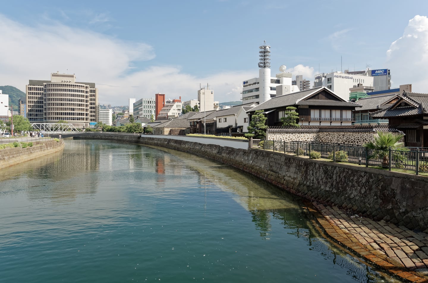 나가사키 데지마, 운하를 따라 늘어선 고풍스러운 복원 건물들과 현대적인 도심 풍경이 어우러진 평화로운 전경입니다.