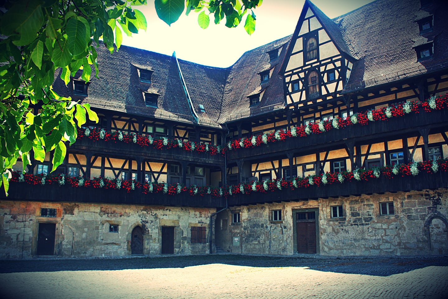 밤베르크 구 궁전, 화려한 꽃 장식으로 꾸며진 하프팀버 양식의 고풍스러운 안뜰 건물과 돌벽이 어우러진 풍경입니다.