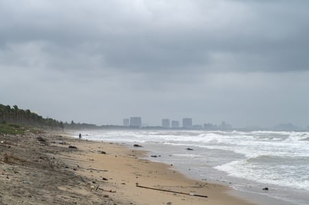 호이안 안방 비치, 먹구름 낀 하늘 아래 거친 파도가 밀려오는 해변과 멀리 보이는 도시의 실루엣이 대조를 이루는 풍경입니다.