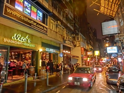 홍콩 소호 거리, 화려한 네온사인 간판 아래로 빨간 택시가 지나가는 활기찬 밤의 레스토랑 골목 풍경입니다.