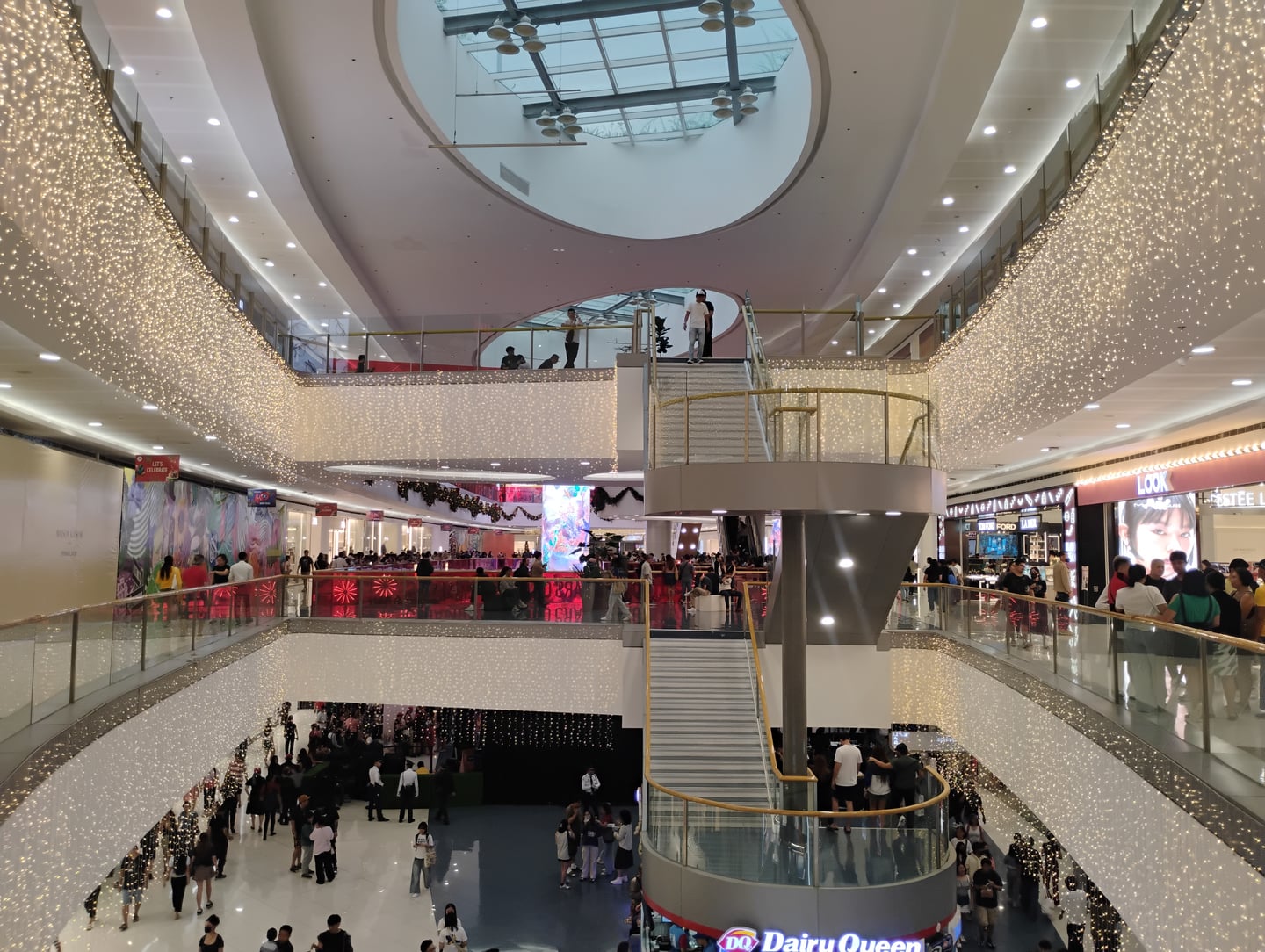 마닐라 SM 몰 오브 아시아, 화려한 전구 장식과 중앙 계단이 어우러진 현대적이고 넓은 쇼핑몰 내부의 활기찬 전경입니다.