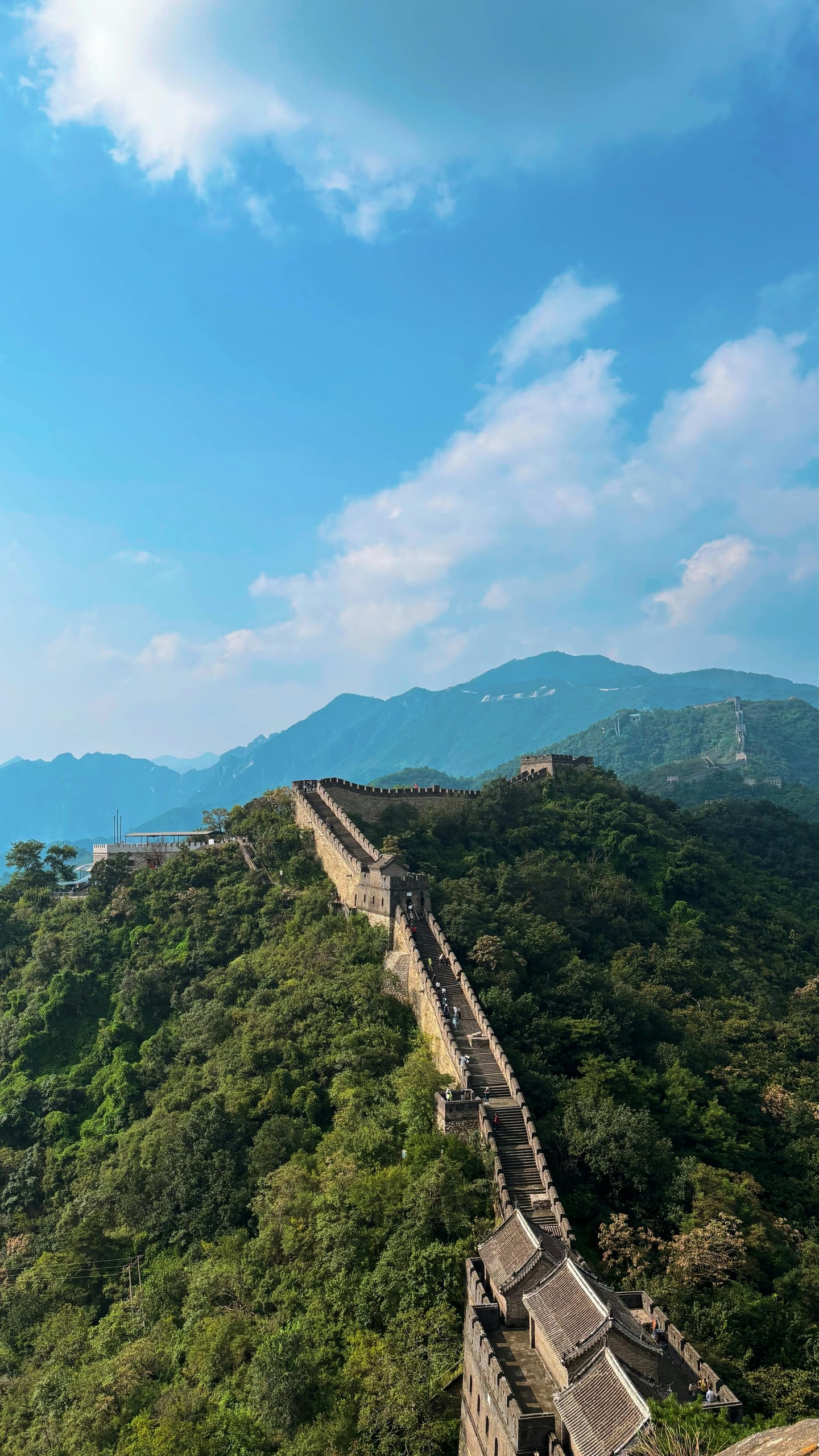 베이징 만리장성, 푸른 하늘 아래 험준한 산등성이를 따라 끝없이 이어지는 고대 성벽과 가파른 계단의 장엄한 풍경입니다.