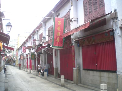 마카오 펠리시다데 거리, 흰 벽과 강렬한 붉은색 목조 문틀이 조화를 이루는 고전적인 중국풍 상점가 골목 풍경입니다.