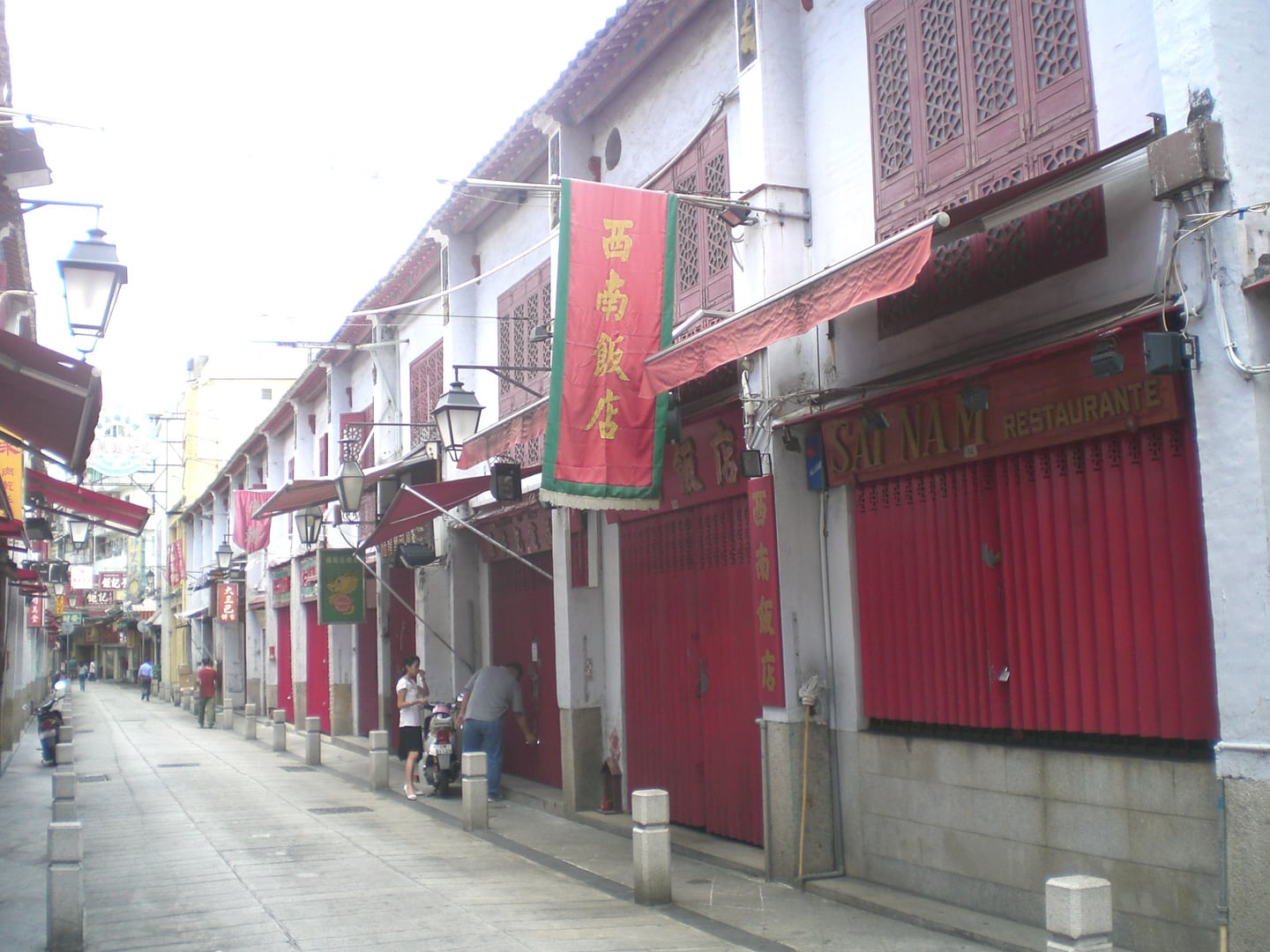 마카오 펠리시다데 거리, 흰 벽과 강렬한 붉은색 목조 문틀이 조화를 이루는 고전적인 중국풍 상점가 골목 풍경입니다.