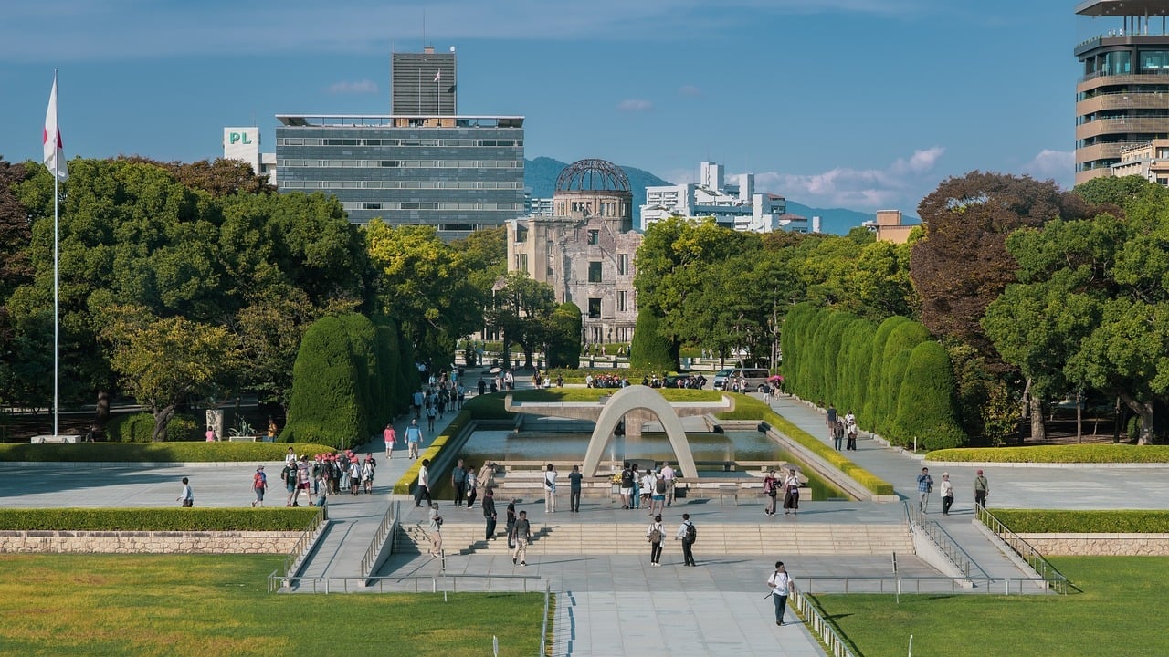 히로시마 평화기념공원, 푸른 나무들 사이로 위령비와 원폭 돔이 일직선으로 보이는 평화로운 공원 전경입니다.