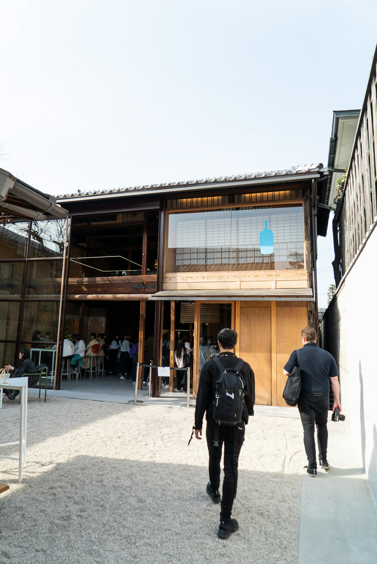 교토 블루보틀 커피, 전통적인 일본식 목조 가옥과 현대적인 통유리창이 어우러진 매장 입구로 향하는 사람들의 모습입니다.