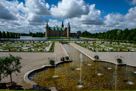 힐레뢰드 프레데릭스보르 성, 화려한 바로크 정원의 분수 너머로 호수 위에 솟아오른 웅장한 르네상스 양식의 성곽 풍경입니다.