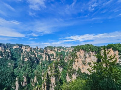 장가계 무릉원 풍경구, 맑고 푸른 하늘 아래 수직으로 솟아오른 거대한 사암 기둥과 푸른 숲이 어우러진 장엄한 자연 경관입니다.