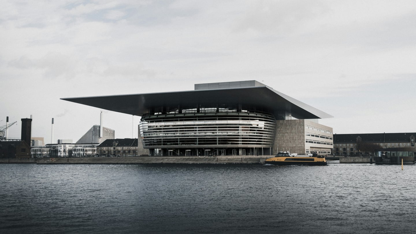 코펜하겐 왕립 오페라 하우스, 운하 위에 떠 있는 듯한 거대한 지붕과 유리 외관이 돋보이는 현대적인 건축물의 전경입니다.