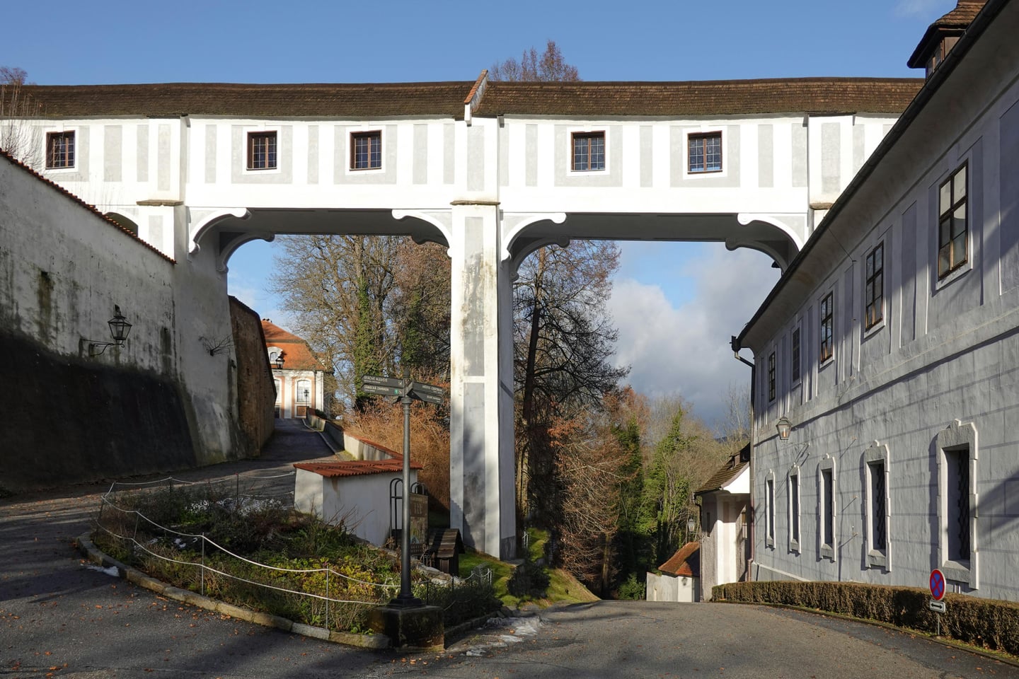 체스키크룸로프 망토 다리, 거대한 흰색 아치 기둥이 도로 위를 가로지르며 성의 구역을 연결하는 웅장한 중세 건축물의 모습입니다.