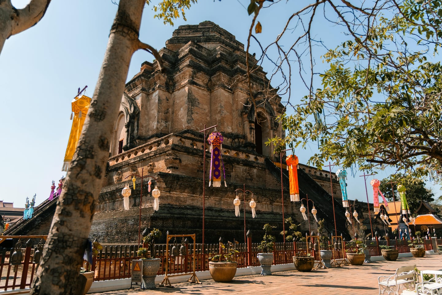 치앙마이 왓 체디 루앙, 푸른 하늘 아래 웅장하게 솟은 고대 벽돌 불탑과 화려한 전통 등불이 어우러진 이국적인 풍경입니다.