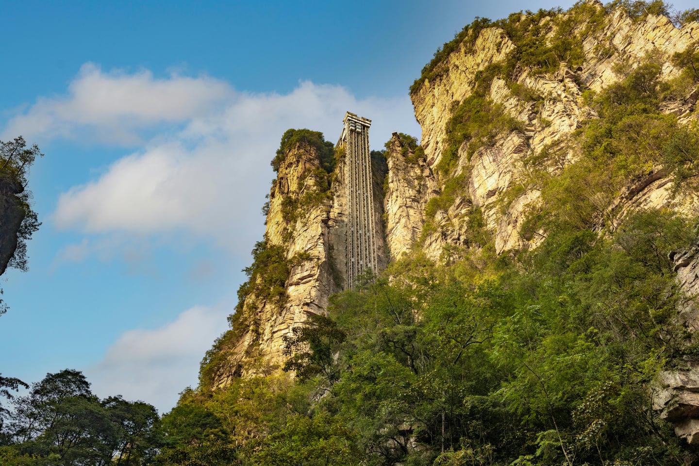 장가계 백룡 엘리베이터, 거대한 수직 절벽을 따라 하늘 높이 솟아오른 세계 최고 높이의 야외 엘리베이터와 웅장한 바위산 전경.