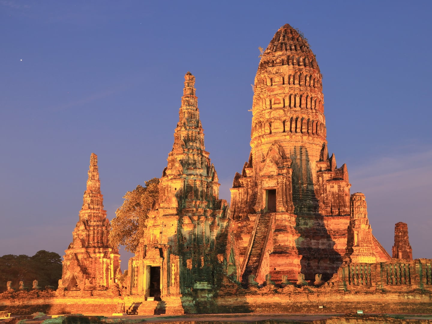 아유타야 왓 차이와타나람, 해 질 녘 황금빛 조명으로 물든 고대 크메르 양식의 거대한 사원 탑과 푸른 밤하늘이 어우러진 풍경입니다.