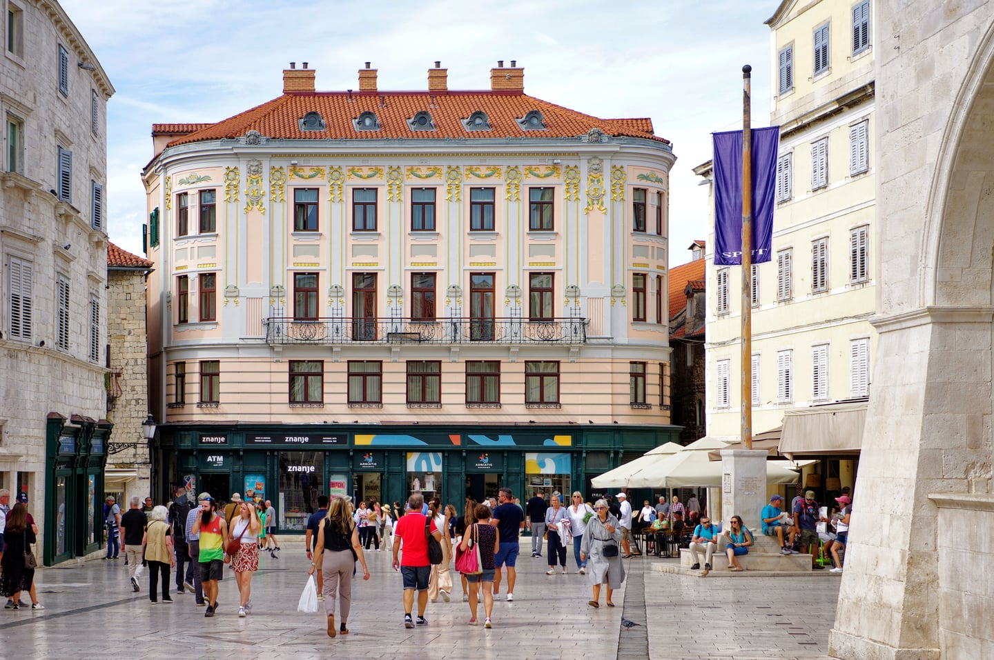 스플리트 나로드니 광장, 고풍스러운 파스텔톤 건축물과 활기차게 광장을 거니는 사람들의 평화로운 오후 풍경입니다.