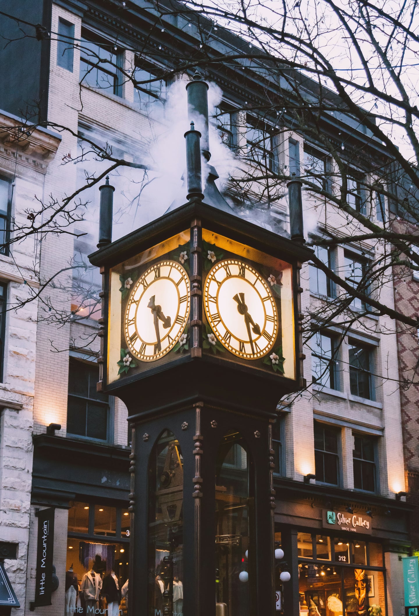 밴쿠버 개스타운, 고풍스러운 건물들 사이에서 하얀 증기를 내뿜으며 따뜻한 빛을 발하는 빈티지한 증기 시계의 야경 모습입니다.