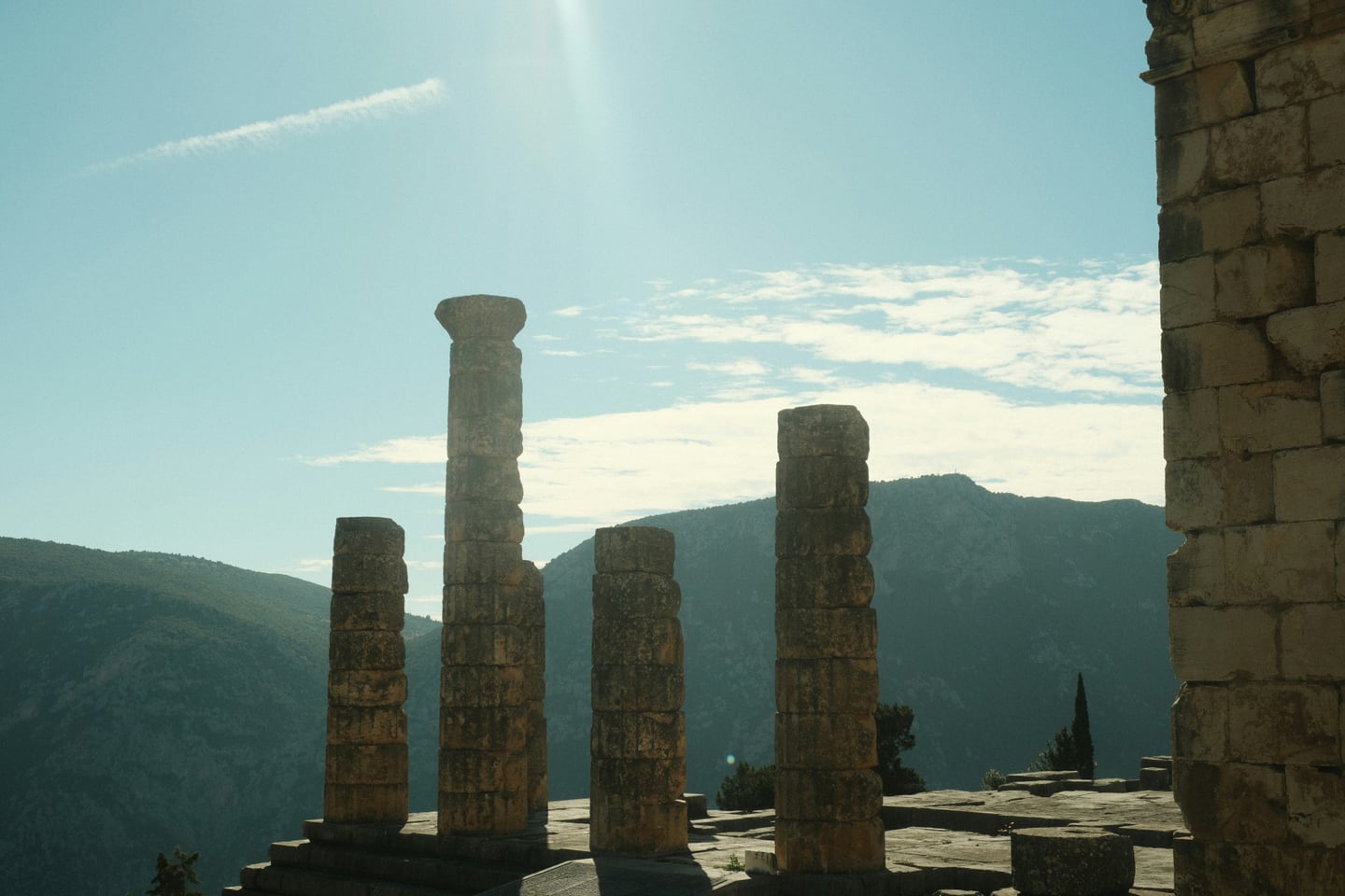 델포이 아폴론 신전, 웅장한 산맥을 배경으로 고대 그리스의 역사를 간직한 도리스식 돌기둥들이 푸른 하늘 아래 장엄하게 서 있는 풍경입니다.