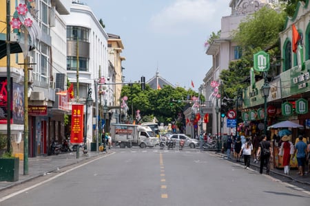 하노이 짱띠엔 거리, 프랑스풍 건축물과 짱띠엔 아이스크림 가게가 늘어선 활기찬 도로 위로 붉은 국기가 펄럭이는 풍경입니다.