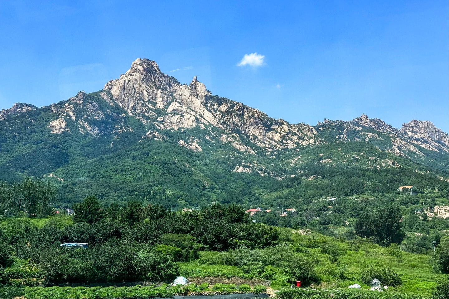 칭다오 노산, 맑고 푸른 하늘 아래 웅장하게 솟아오른 거대한 화강암 봉우리와 울창한 숲이 어우러진 장엄한 풍경입니다.