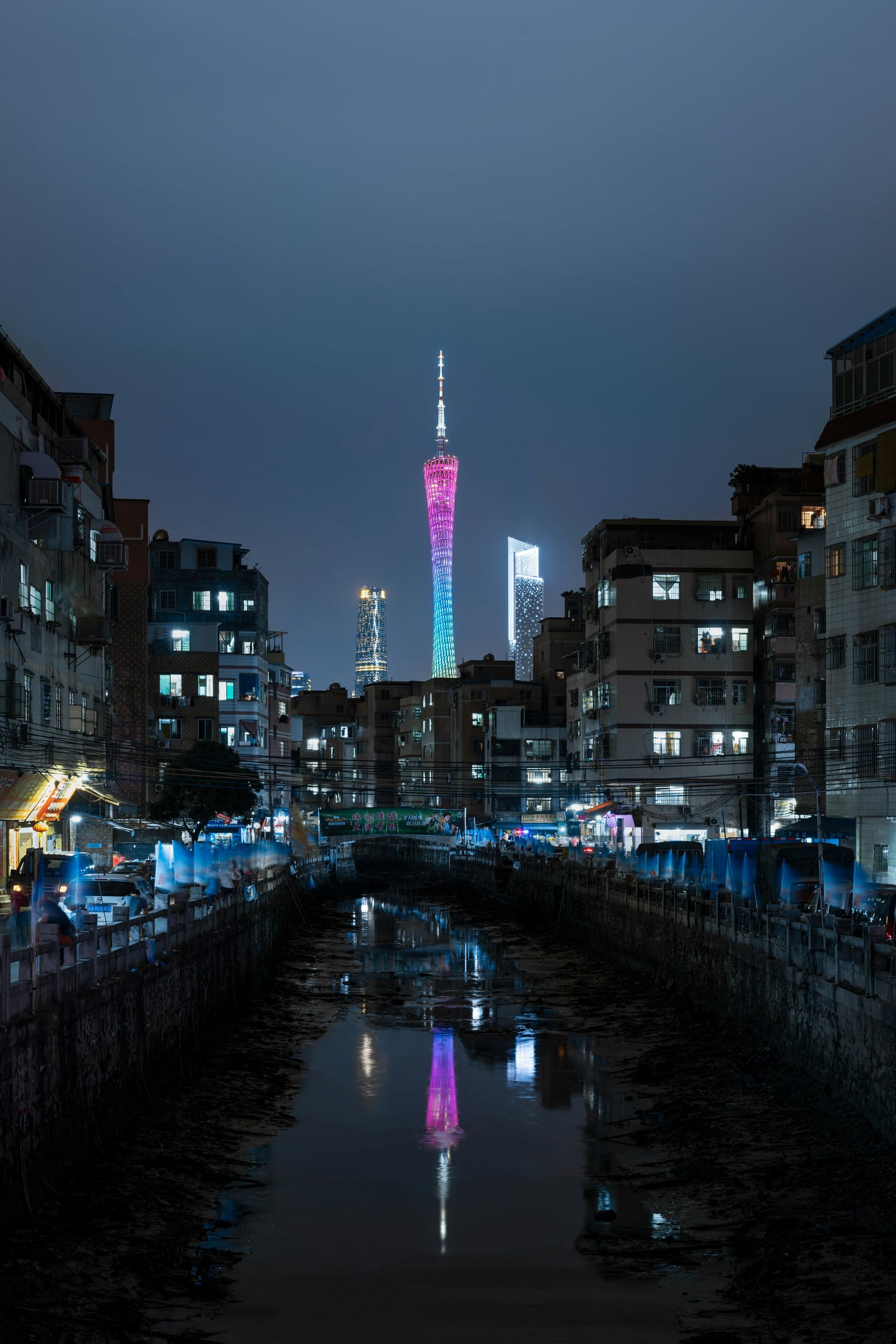 광저우 광저우 타워, 오래된 도심 건물들 사이로 보이는 화려한 무지개색 조명의 타워와 운하에 비친 야경 반사.