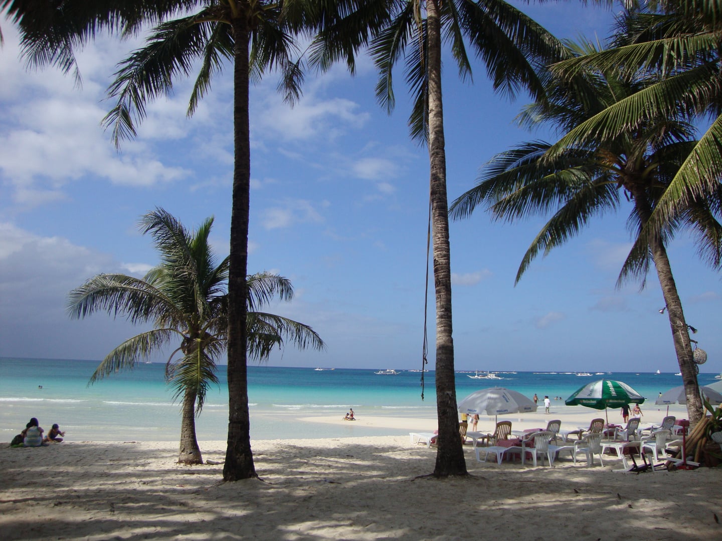 보라카이 화이트 비치, 야자수 그늘 아래 펼쳐진 투명한 에메랄드빛 바다와 평화로운 해변의 선베드 풍경입니다.