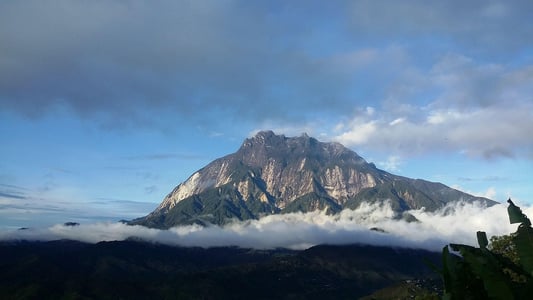 코타키나발루 키나발루 산, 구름 위로 솟아오른 거대한 암벽 봉우리와 푸른 하늘이 어우러진 장엄한 풍경입니다.