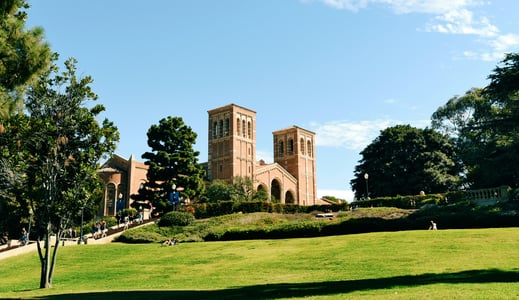 로스앤젤레스 UCLA, 푸른 잔디 언덕 너머로 보이는 웅장한 로이스 홀의 붉은 벽돌 외관과 평화로운 캠퍼스 풍경입니다.