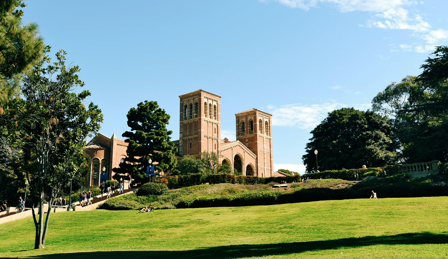 로스앤젤레스 UCLA, 푸른 잔디 언덕 너머로 보이는 웅장한 로이스 홀의 붉은 벽돌 외관과 평화로운 캠퍼스 풍경입니다.