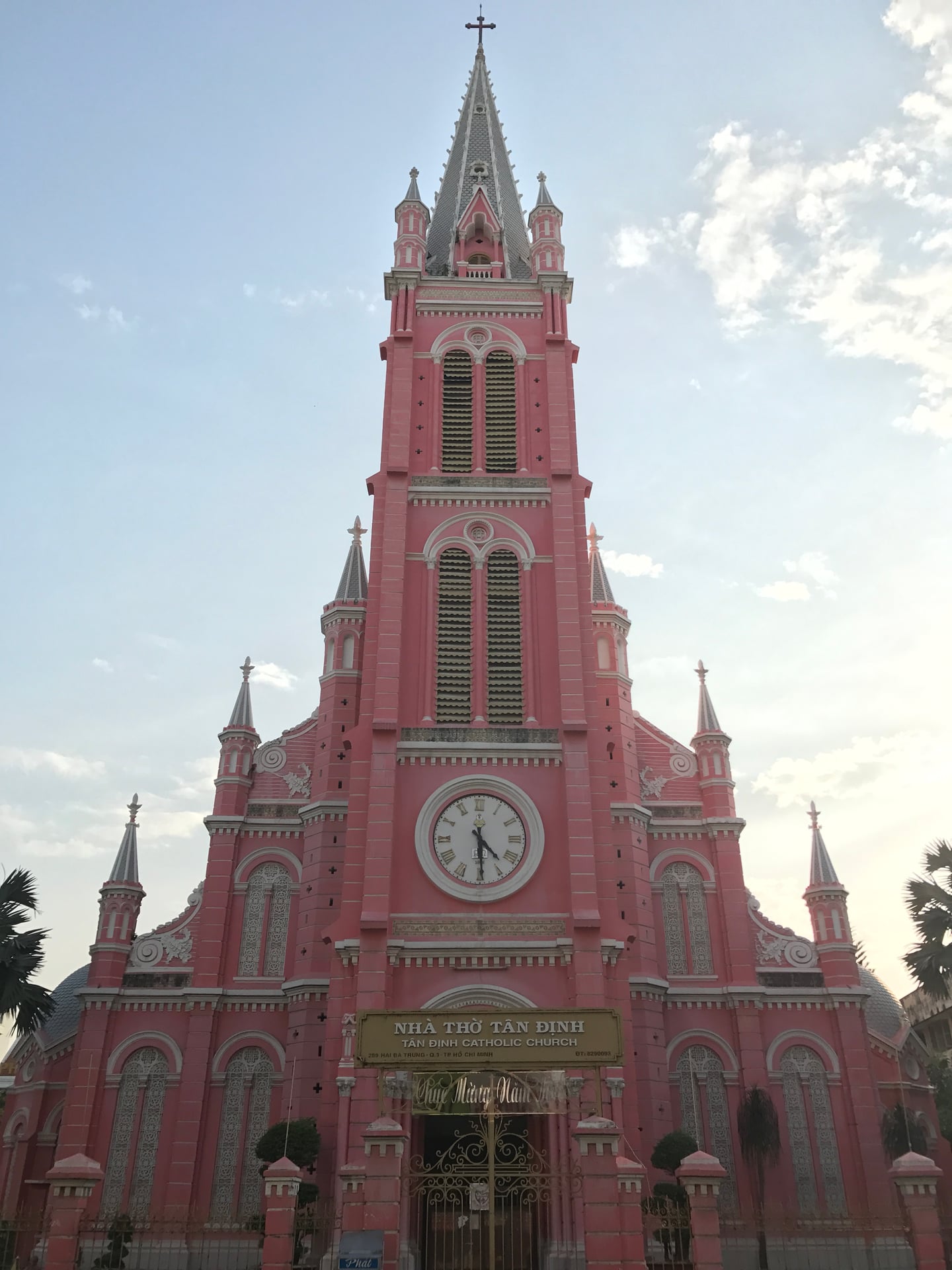 호치민 떤딘 성당, 푸른 하늘 아래 우뚝 솟은 화려한 분홍색 외벽과 정교한 시계탑이 돋보이는 고딕 양식의 건축물입니다.