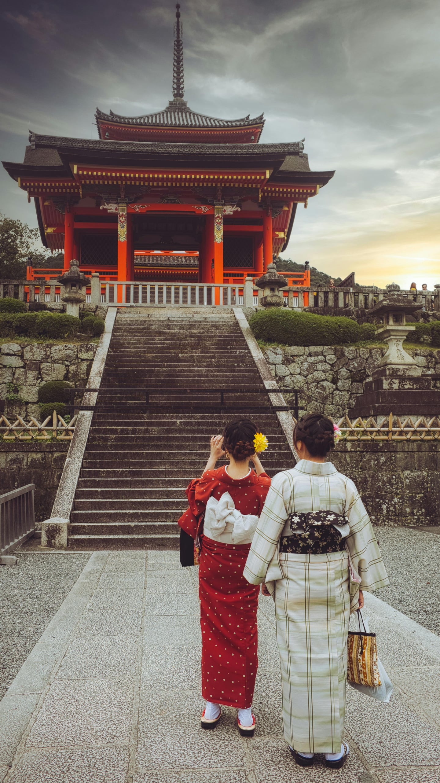 교토 청수사, 화려한 붉은색 인왕문과 석조 계단을 배경으로 전통 기모노를 차려입은 두 여성이 사찰의 정취를 감상하는 뒷모습입니다.