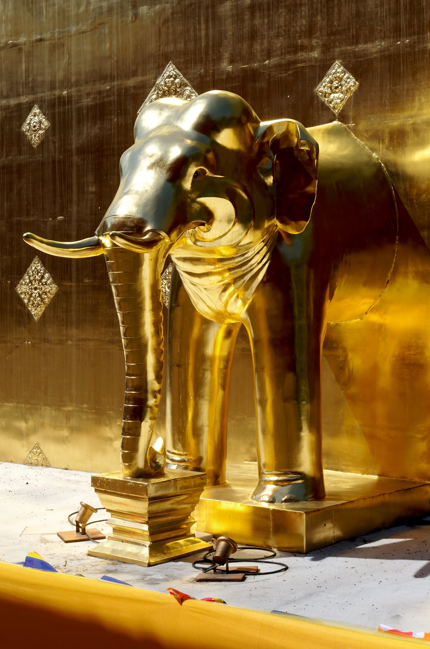 치앙마이 왓 프라싱, 황금빛 벽면을 배경으로 찬란하게 빛나는 정교한 코끼리 조각상이 태국 불교 예술의 화려함을 자아냅니다.