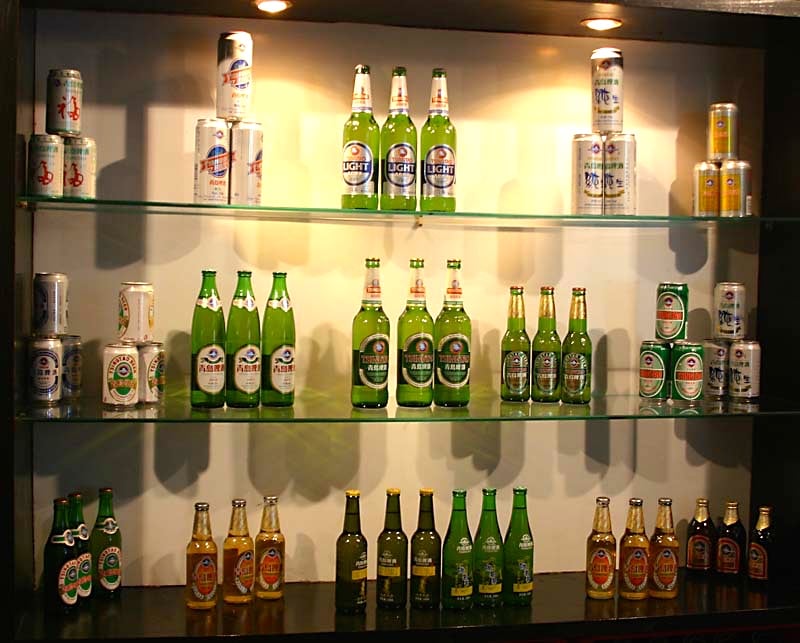 칭다오 칭다오 맥주 박물관, 박물관 내부 유리 진열장에 시대별로 다양하게 전시된 칭다오 맥주 병과 캔의 모습입니다.