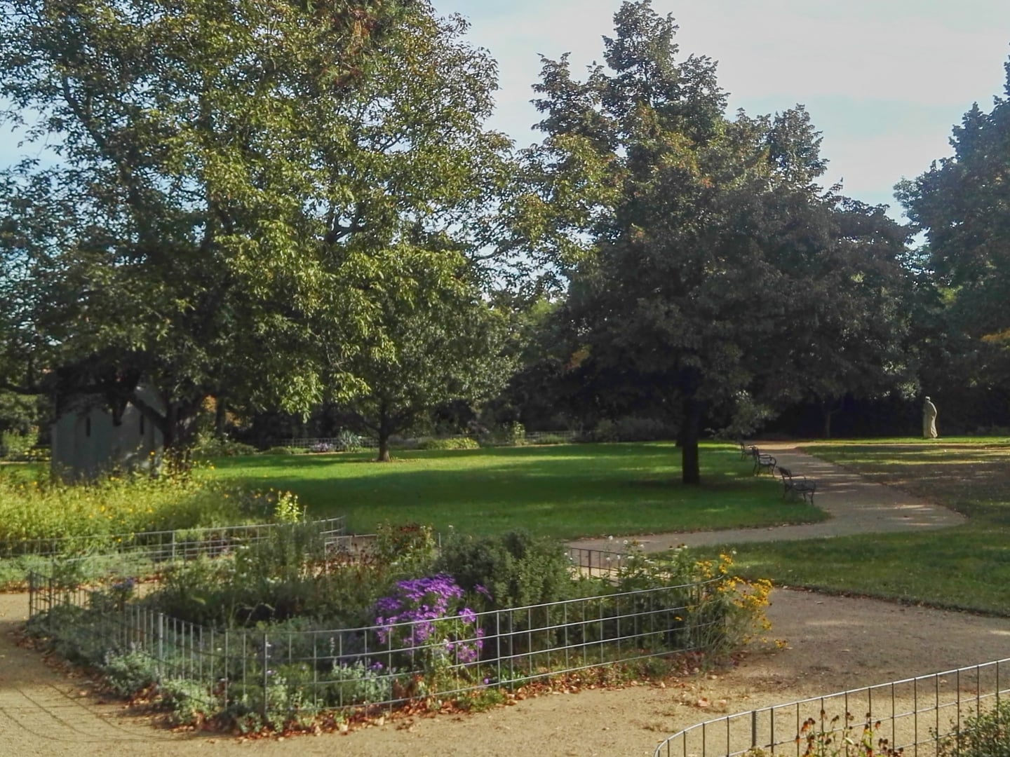 프라하 비셰흐라드 공원, 푸른 잔디밭과 보라색 꽃이 핀 화단 사이로 굽이진 산책로가 평화롭게 펼쳐진 모습입니다.