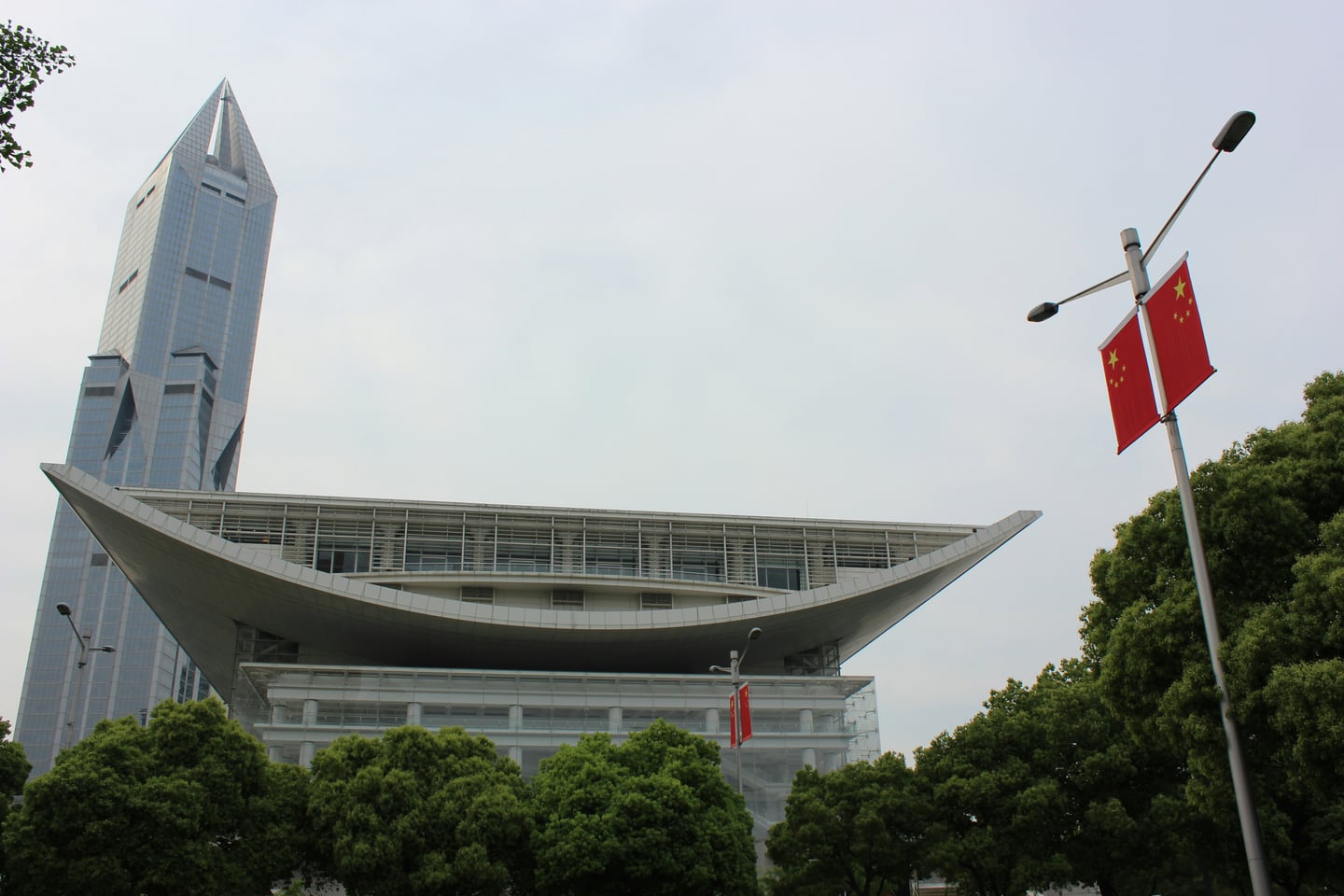 상하이 상하이 대극원, 거대한 곡선형 지붕이 돋보이는 현대적 건축물과 그 뒤로 높게 솟은 마천루가 조화를 이루는 풍경입니다.