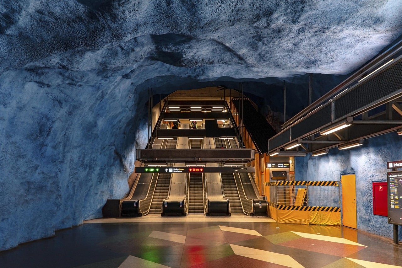스톡홀름 지하철역, 푸른색 암반 동굴 천장 아래로 길게 뻗은 에스컬레이터와 기하학적 무늬의 바닥이 어우러진 예술적인 역사 내부 전경입니다.